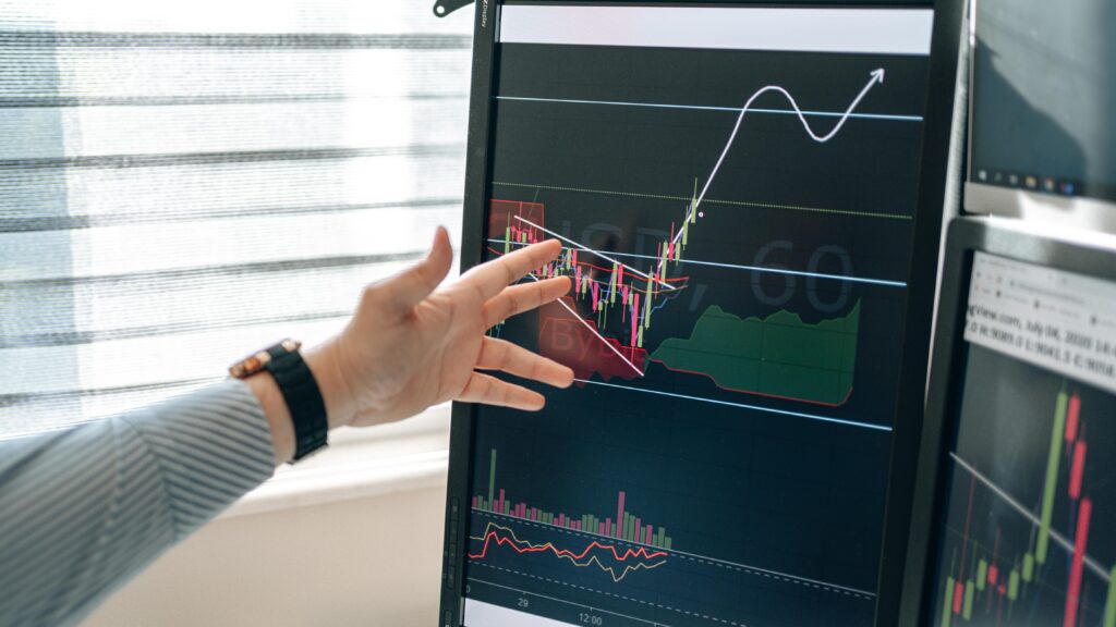 Financial analyst pointing to an upward stock market trend chart on a vertical trading monitor demonstrating AI wealth management growth.