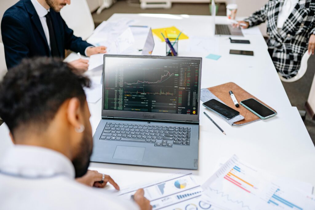 Financial analysts monitoring stock market candlestick charts on a laptop during an institutional capital investment meeting.